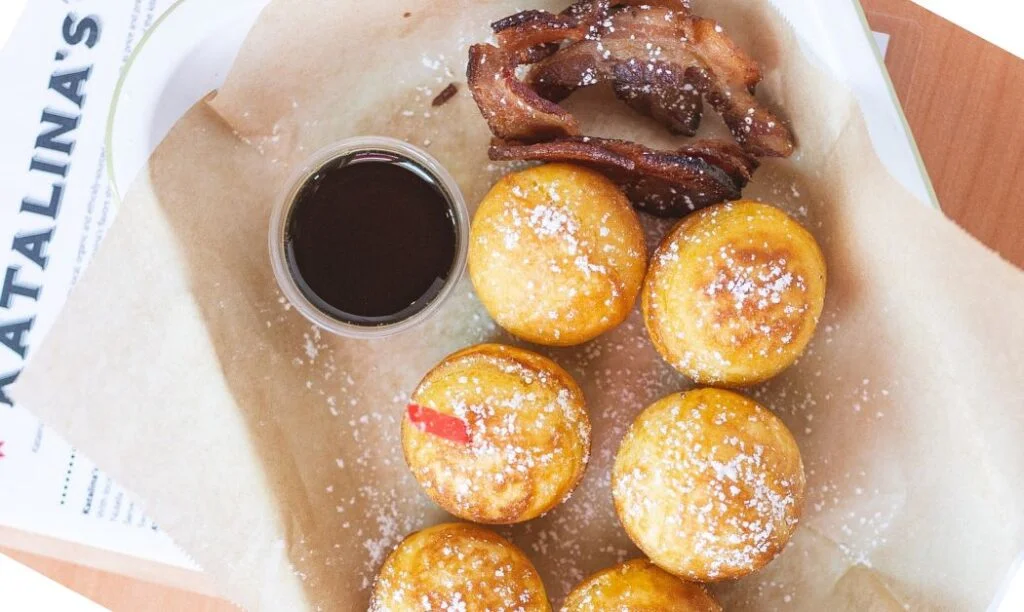 Katalina's famous pancake balls lightly dusted with powdered suger, accompanied by syrup, and bacon.