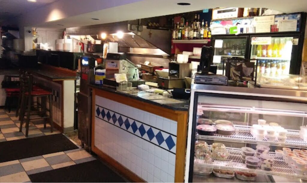 Interior photo of Apollo's counter featuring their case, bar seating, register, and grill.