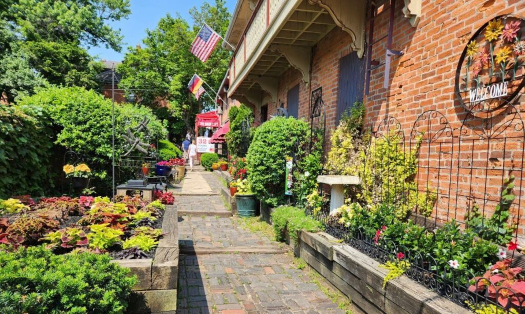 The Book Loft of German Village's outdoor courtyard with lots of flowers, a brick path, and an old school brick building. 