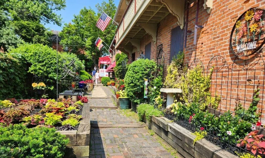The Book Loft of German Village's outdoor courtyard with lots of flowers, a brick path, and an old school brick building.