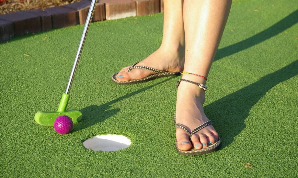 Woman putting a purple ball into a mini golf hole.