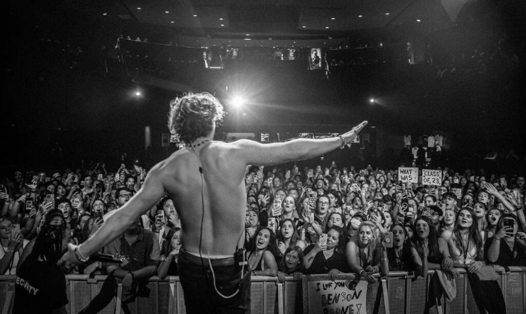 Benson Boone performing to an audience as a spotlight shines on him.