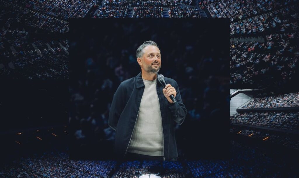 Comedian Nate Bargatze performs in front of a large arena audience.