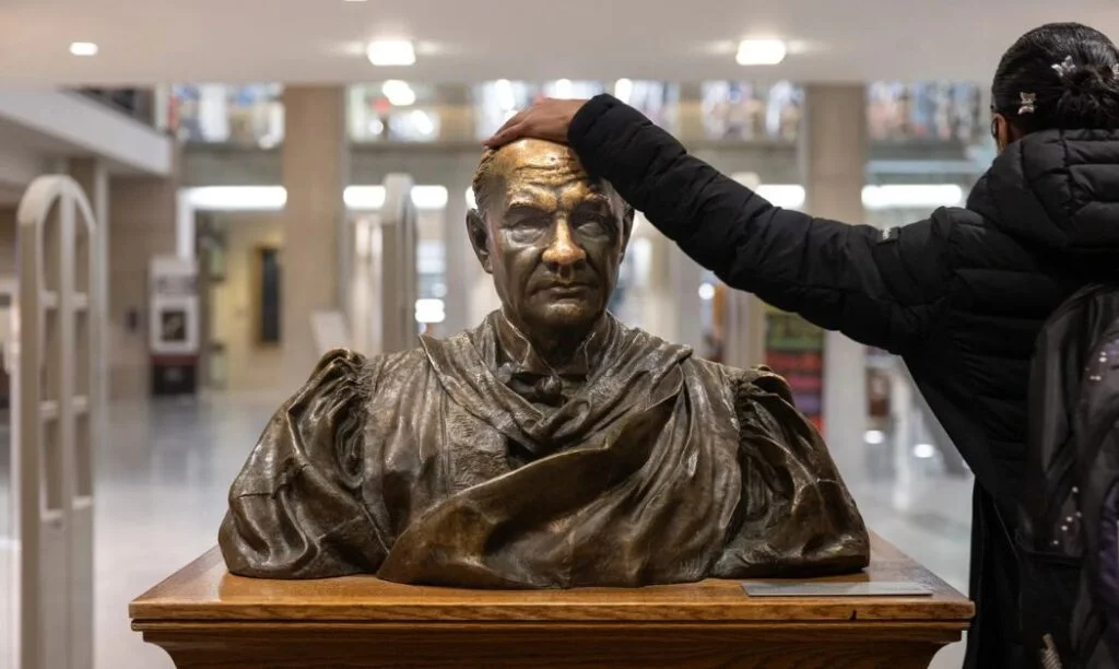 A student rubbing the head of the bust of William Oxley Thompson at Thompson Library on Ohio State's campus