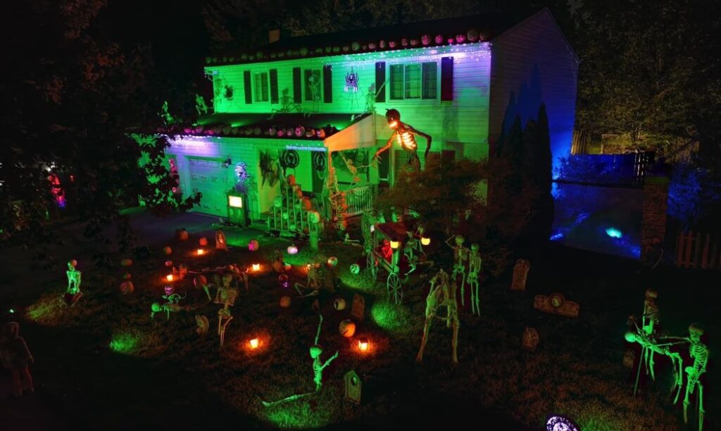 A house lit up in green and Halloween decorations like lanterns, a giant skeleton, and more.