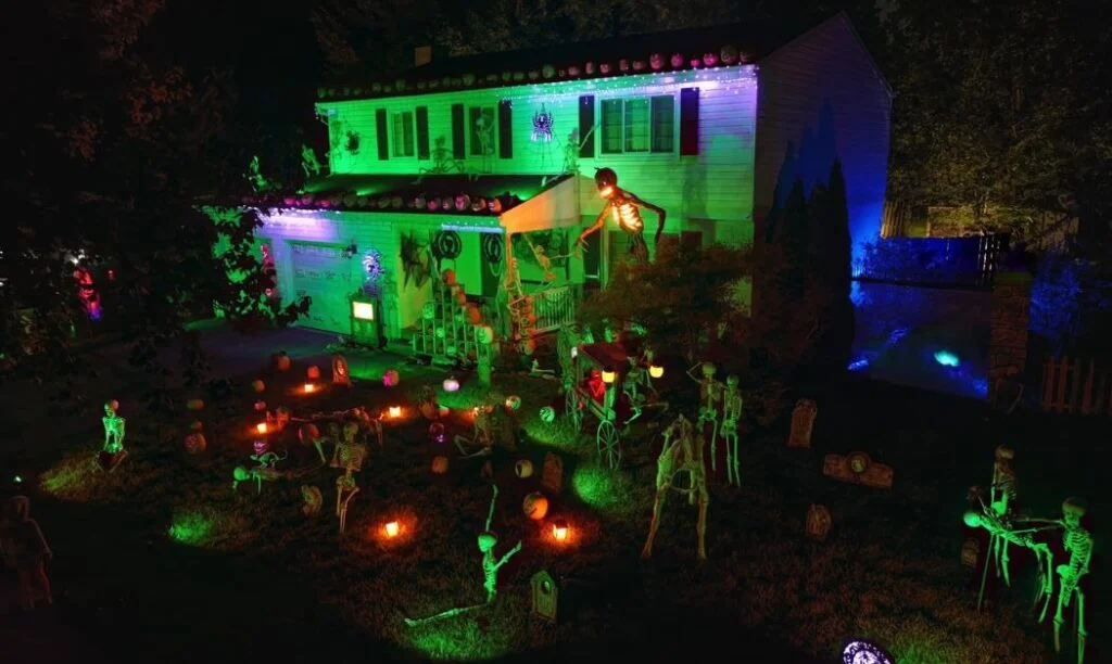 A house lit up in green and Halloween decorations like lanterns, a giant skeleton, and more.