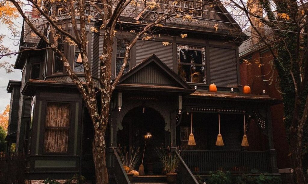 A Gothic-style home in the Victorian Village neighborhood of Columbus, OH during autumn, with pumpkins on the roof and broom sticks hung from the porch.